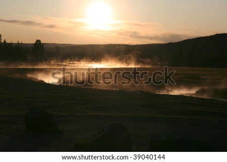 Early morning sun shining through the mist rising from a river winding through grass land in Yellowstone National Park.