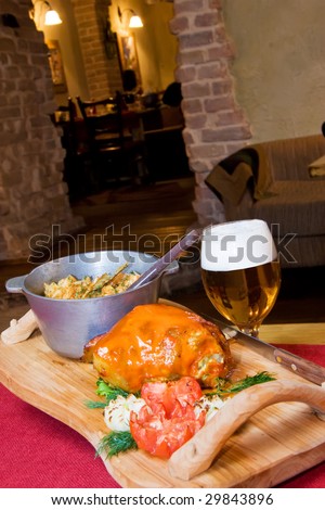 A closeup view of a variety of cooked food on a wooden tray and a glass of beer in a cozy setting.