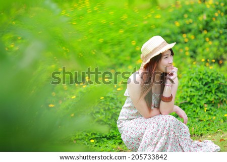 Asian beautiful young girl,wear floral maxi dress and hat, sitting on the ground at spring