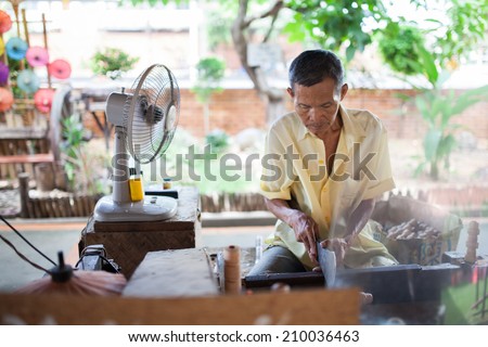 old  asian man yellow shirt sitting, making a wooden umbrella in traditional umbrella factory