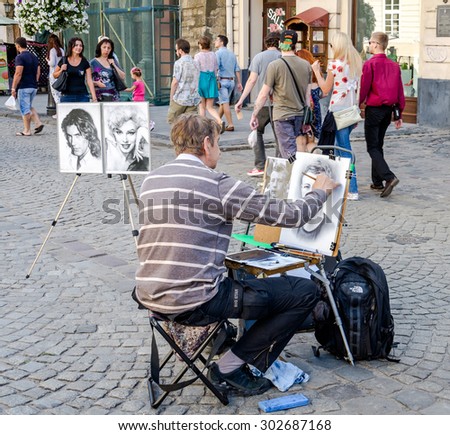 Lviv, Ukraine - July 2015: Male street artist draws a portrait of a man with a brush on the canvas in Lviv, at Market Square