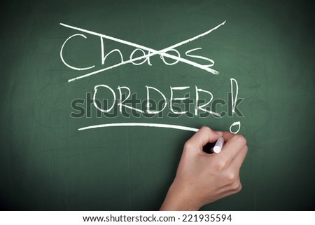 Chaos or Order / Hand Crossed out Chaos Word and Writing Order on chalkboard