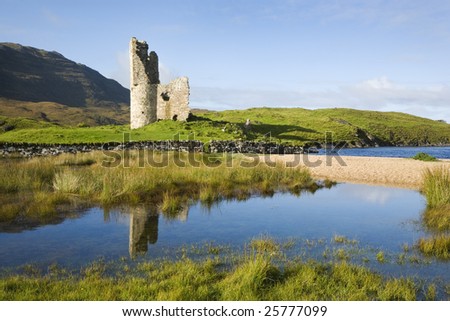 Ruin of ancient Scottish castle with pools of water and green grass in front and blue sky in the background