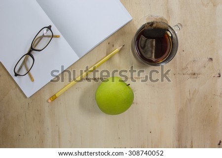 green apple, pencil, glasses, tee and notebook on wooden