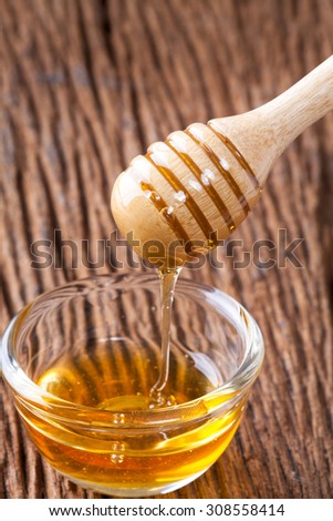 Honey bowl with dipper and flowing honey on the wood table