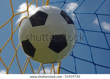 the foot ball in mesh of goal on background of clouds