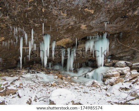 Group icicles hang down from a shelf in a cave on a background of stones