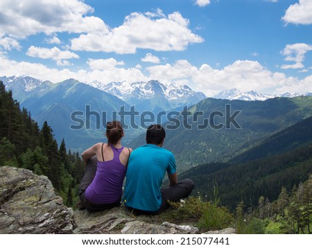 Love couple sitting on the edge of the rocks on the background of mountains with snow