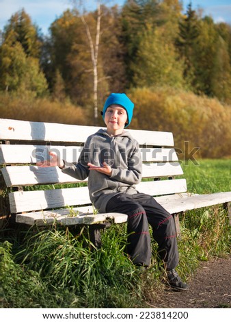 Lonely boy sitting on a bench in a cap and jacket and he invited to sit next to him