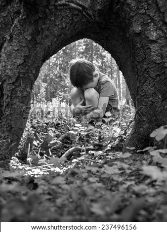 Monochrome image of a little boy lost in the woods and sits having embraced her legs