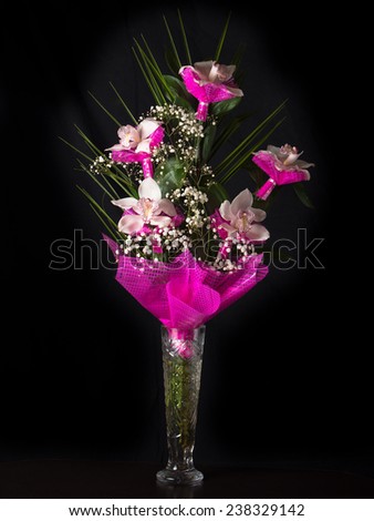 Bouquet of orchids stands in a glass vase on a black background