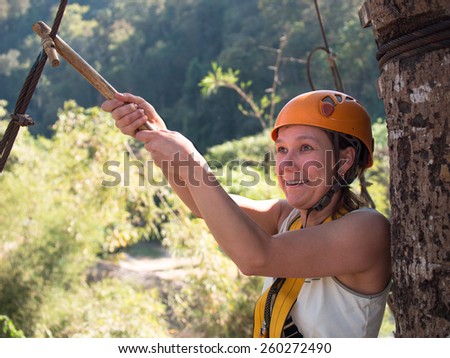 Adult woman in a helmet and with a frightened face holding on to an iron cable before jumping on a blurred background