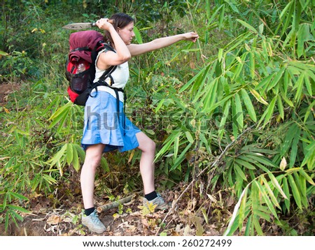 Adult woman with a backpack and a large knife is paving the way in the jungle