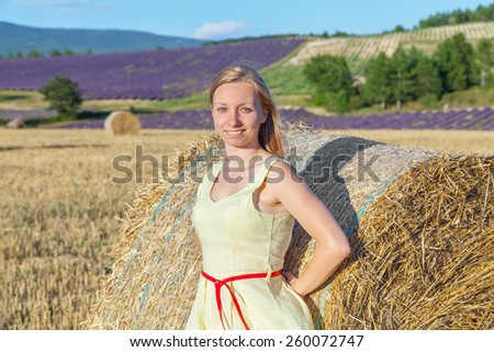 A smiling lady in a yellow dress with red belt near the bale of straw on a background of the rural landscape in Provence, France