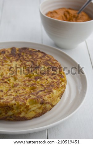 Spanish Omelet also known as Spanish Tortilla on White Wooden Table with romesco sauce in the background