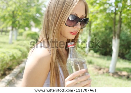 Portrait of beautiful smiling woman in sunglasses with bottle of water in hands, closeup shot, outdoors, summer