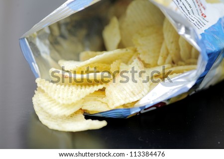 Opened pack of delicious spicy potato chips over black  table