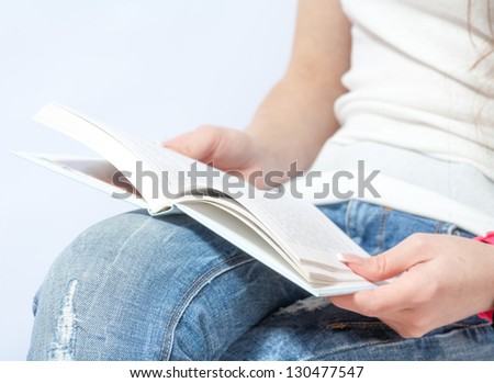 Cropped close-up of woman sitting cross-legged and reading a book. Vertical format.
