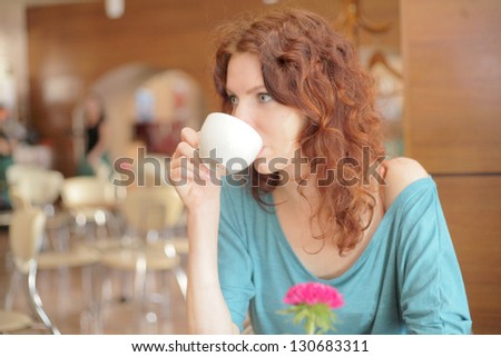 Redhead woman with curly hair drinking coffee from a cup shallow depth of field
