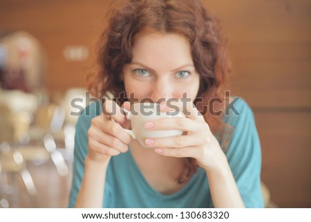 Redhead woman with curly hair drinking coffee from a cup shallow depth of field