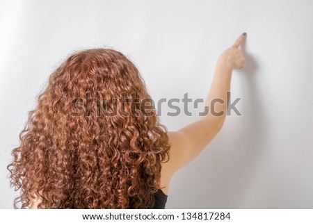Back view of young woman in jeans and  black shirt points at wall. Rear view