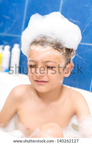 Cute three year old boy taking a bath with foam closed eyes, foam on the head