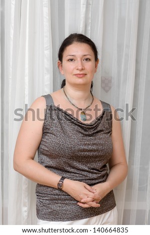 Beautiful brunet mature woman relaxing - pretty mid age woman relaxing at home lookinf at camera, vertical shot, against curtains