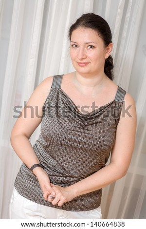 Beautiful brunette mature woman relaxing - pretty mid age woman relaxing at home lookinf at camera, vertical shot, against curtains