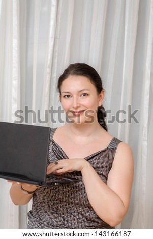 Mid age business woman using laptop - mid age brunette women with small laptop in hands indoors smiling