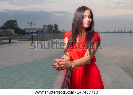 Fashion portrait of pretty sexy classy brunette in red shiny dress and long straight hair . vertical shot against sky, outdoors. luxury photography.