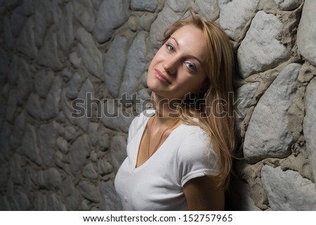 Closeup of Beautiful blonde woman head and shoulders relaxing near the wall in the evening, looking at camera and smiling