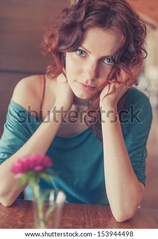 Vintage toned cross process colors version Redhead women sitting in the cafee with pink flower on the table befor and looking at camera and smiling