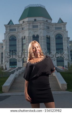Beautiful blond woman walking alone outdoors at night posing against big building