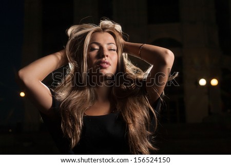 Beautiful blond 20s female posing alone outside at night with hands in her beautyful hair
