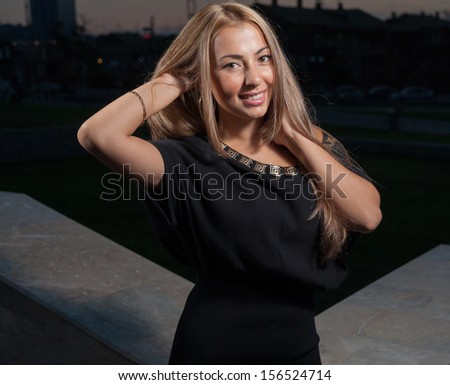 Beautiful blond woman smiling and posing in fashion manner alone outdoors at night