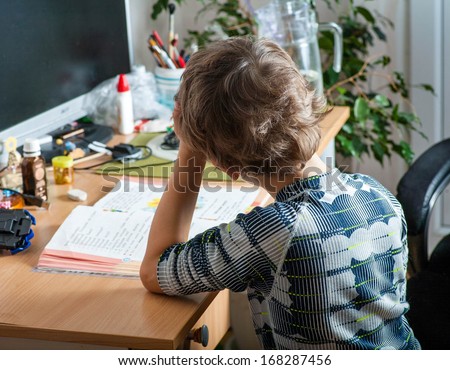 Little boy sitting rely on hand. Back view of schoolchildren studying at home