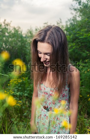 Female looking down and smiling. Beautiful Young Woman standing in Meadow of Flowers.
