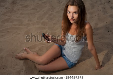Women with cell phone sitting on sand and looking at camera