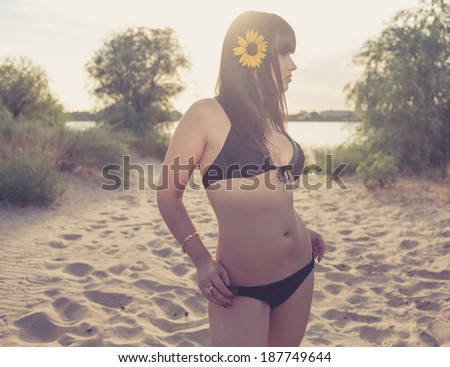 Bikini women standing on sandy beach with sunflower in her pretty long hair
