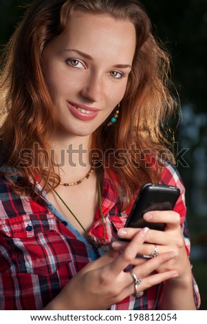 Carrot-top women (redhead) communicate via cell phone. Cute women looking at camera and smiling with mobile phone in her hands.