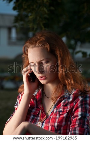 Red haired women call by cell phone outdoors and looking down