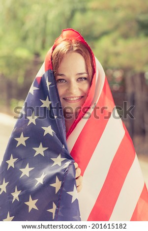 Smiling girl covered with US flag outdoors vertical shot