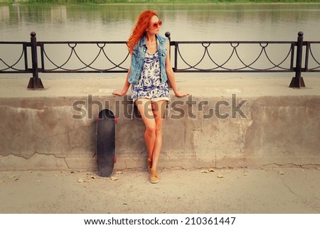 Beautiful and fashion young woman posing with a skateboard leaning river parapet