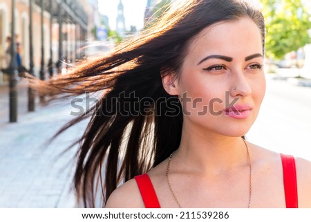 Young long haired brunette outdoor headshot. Pretty women with serious face looking away with hairs fly by the wind