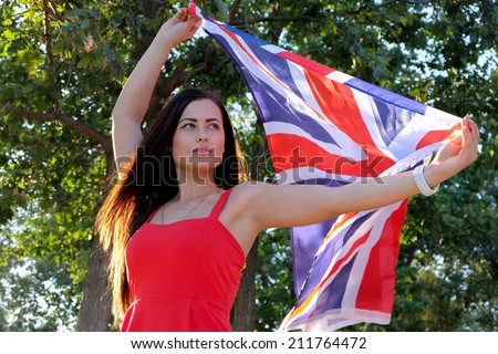 Young brunette holding UK flag in her outstretched hands, flag fly by the wind