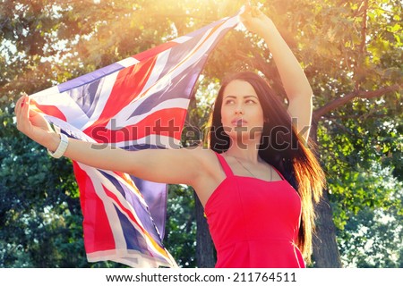 Young brunette holding UK flag in her outstretched hands, flag fly by the wind