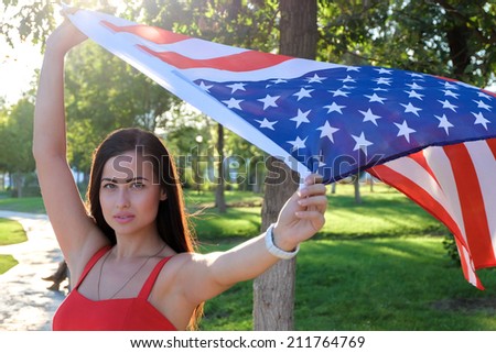 Serious young woman holding american flag flying by the wind
