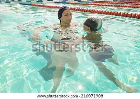 Son and mother in swimming pool. Mom giving son a swimming lesson in pool during summer.