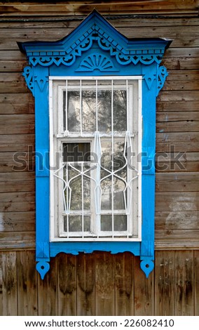 Blue window in traditional tribal Russian style on facade of ancient wooden slum house