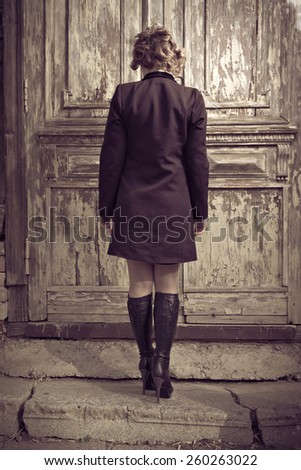 Rear view of beautiful girl in a coatagainst weathered door in the city, loneliness, depression concept.